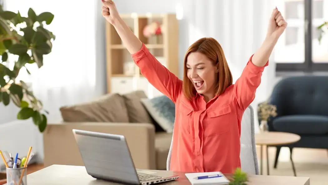 A woman sat at her laptop looking happy and cheering