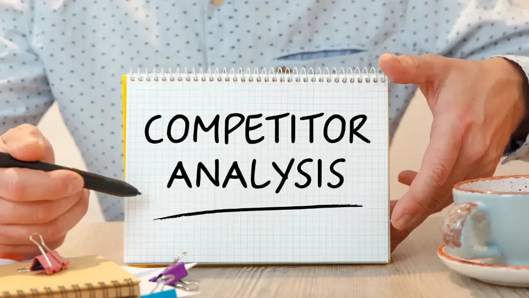 A man holding a pen and notepad that says "competitor analysis"