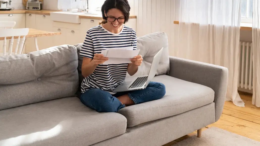 A woman sat on a sofa smiling whilst opening a letter