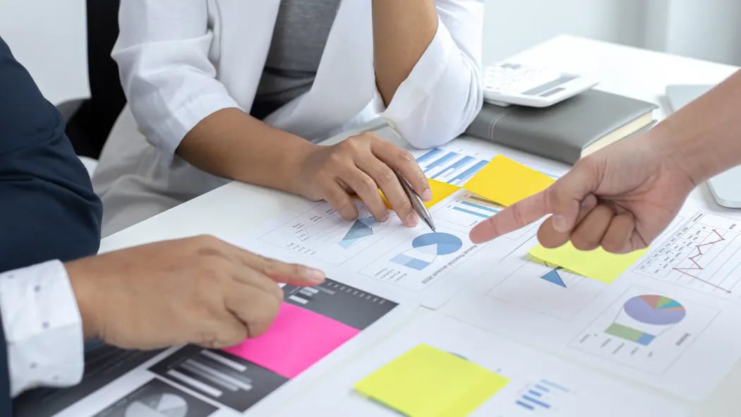 Hands hovering over a desk that has graphs and data on sheets of paper