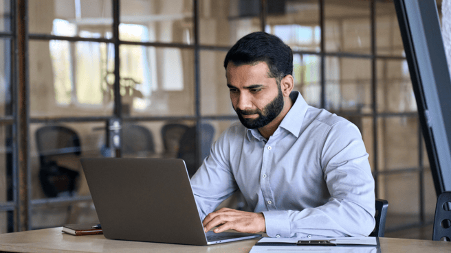 a man sitting an an office desk working on a laptop