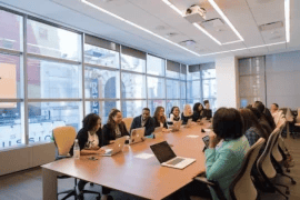 Ten or more people sat around a wooden conference table having a meeting