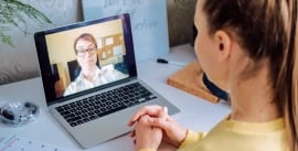 One woman at a desk having a virtual meeting with another woman shown on a laptop screen
