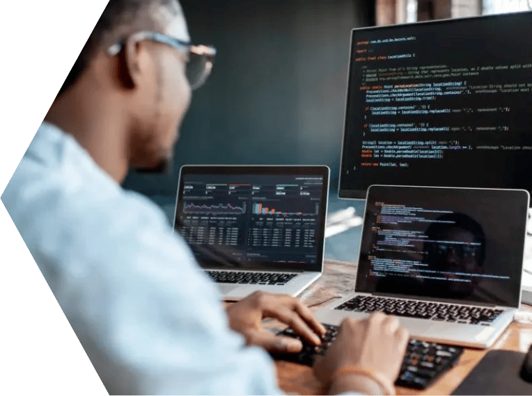 Man sat at a desk in front of three computer screens displaying computer code