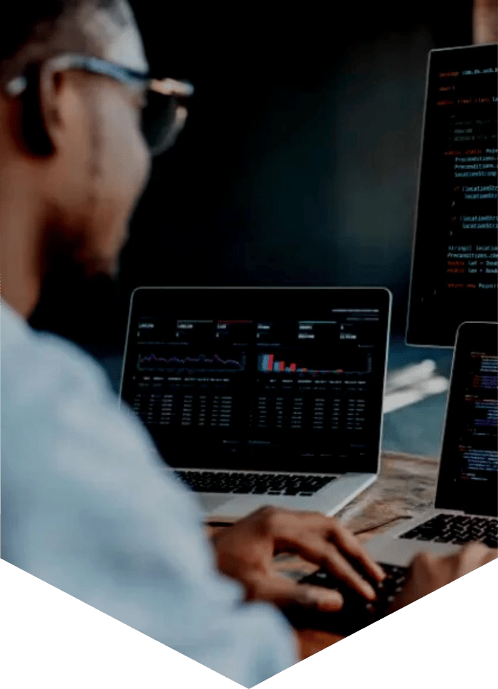 Man sat at a desk in front of three computer screens displaying computer code