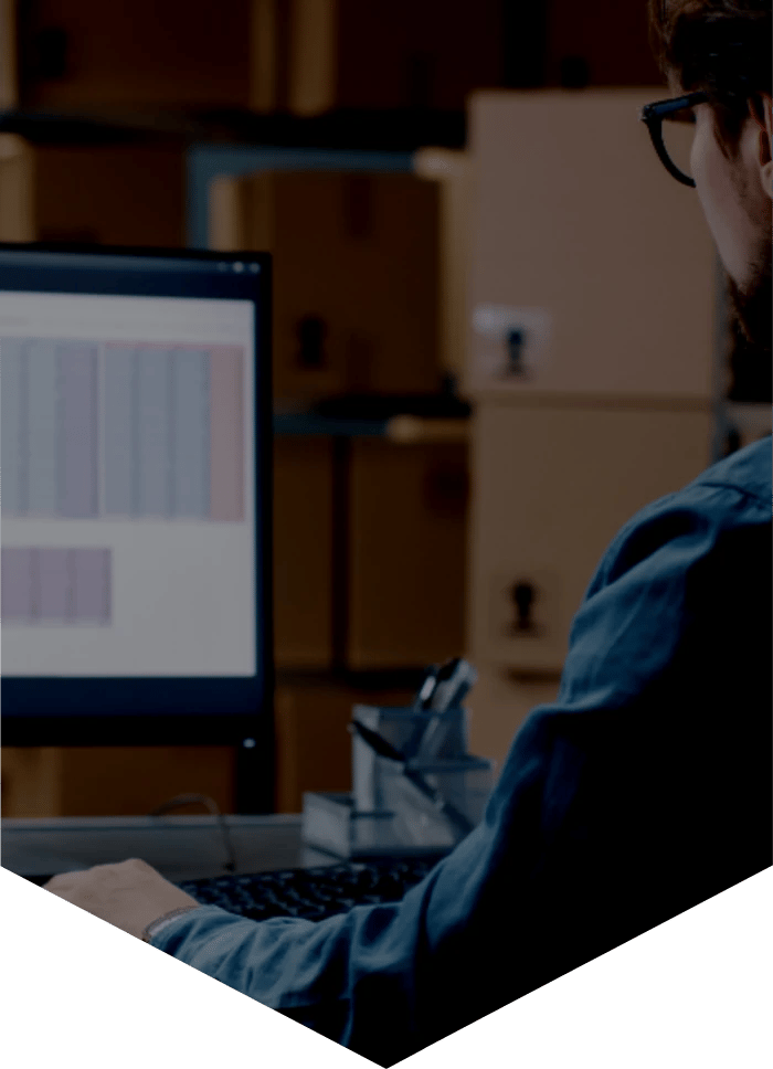 Man sat in front of a desktop computer screen that's displaying a spreadsheet of data