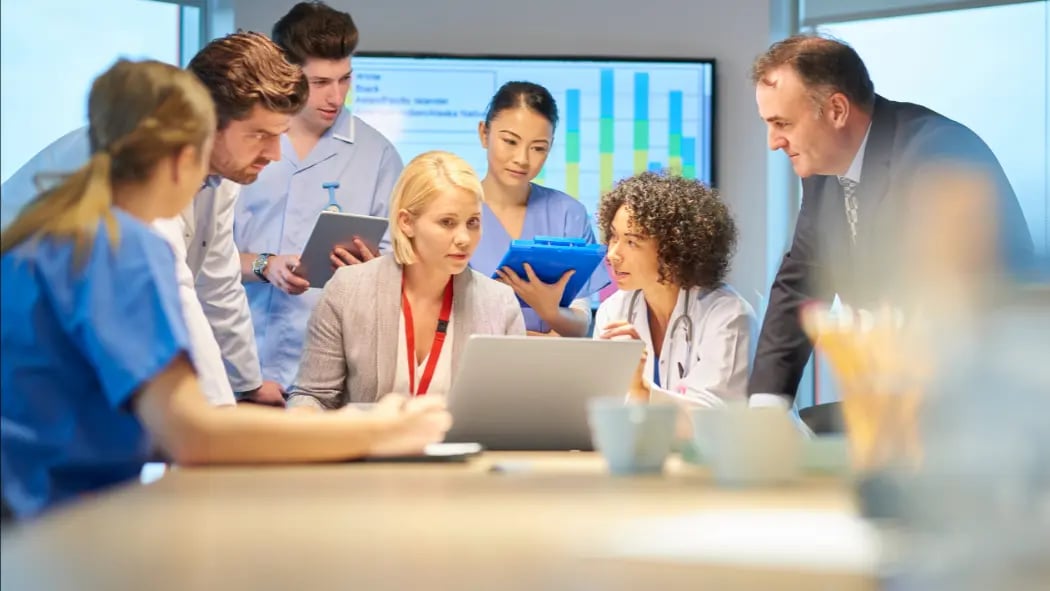 Doctors and nurses surrounding a person on a laptop in a meeting
