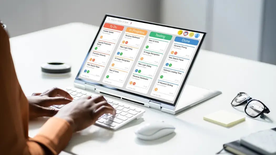Hands typing on a keyboard with a tablet screen showing projects being organised into a chart