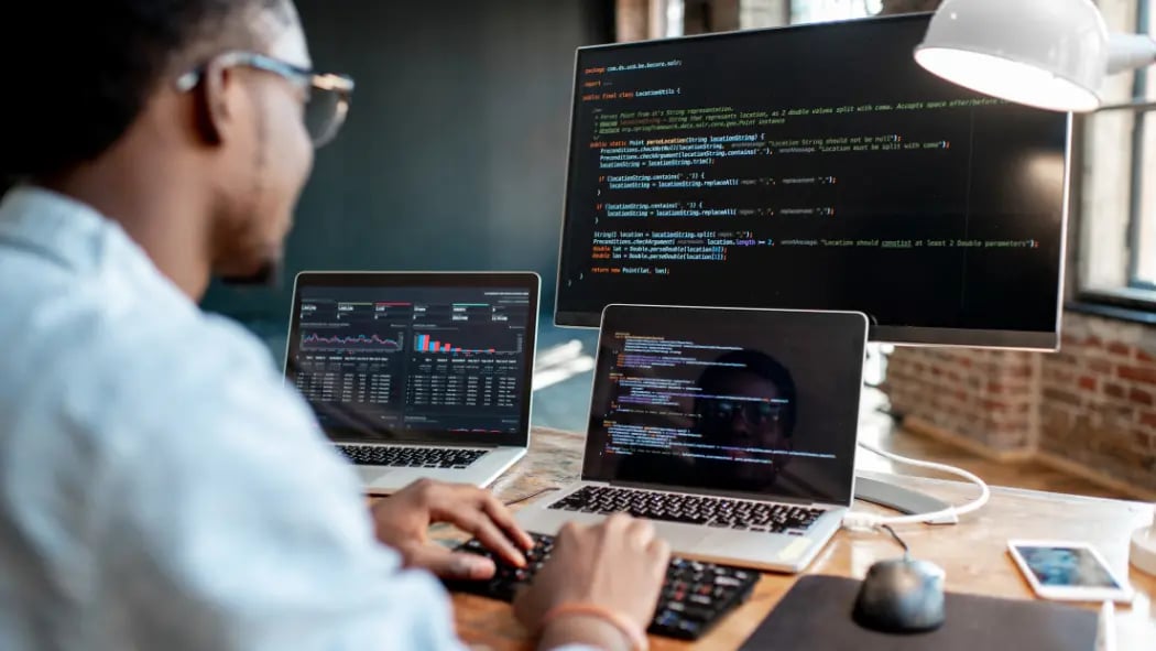 Man sat at desk with 3 computer screens showing Python
