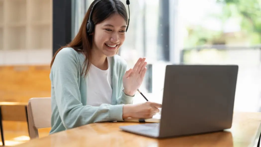 Woman sat with headphones on at laptop waving at the screen