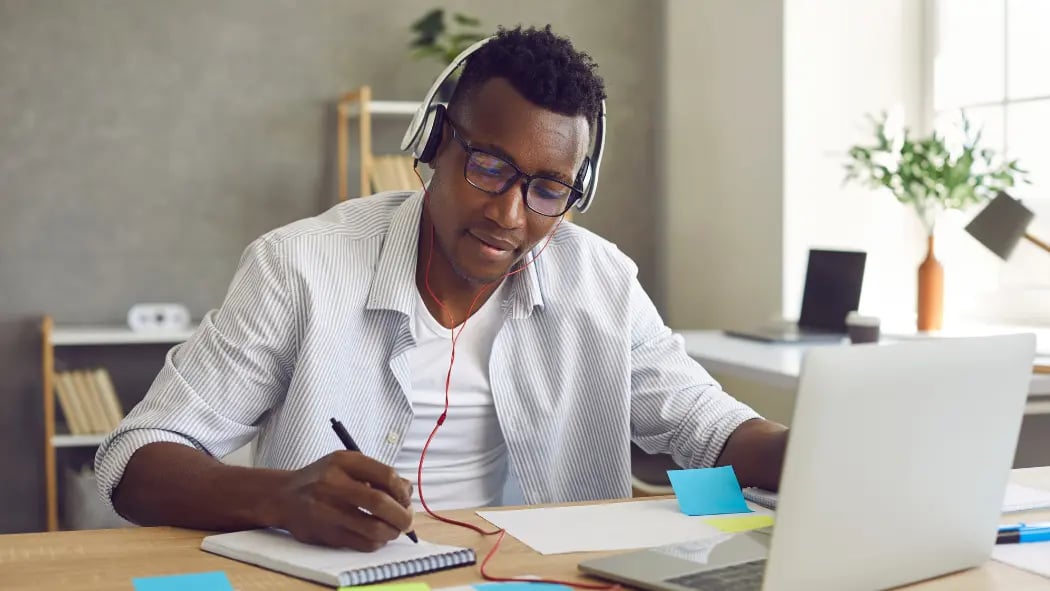 a man working at his desk and laptop with headphones on 