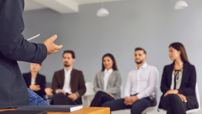 People sitting in a group at work setting listening to leader at the front of the room